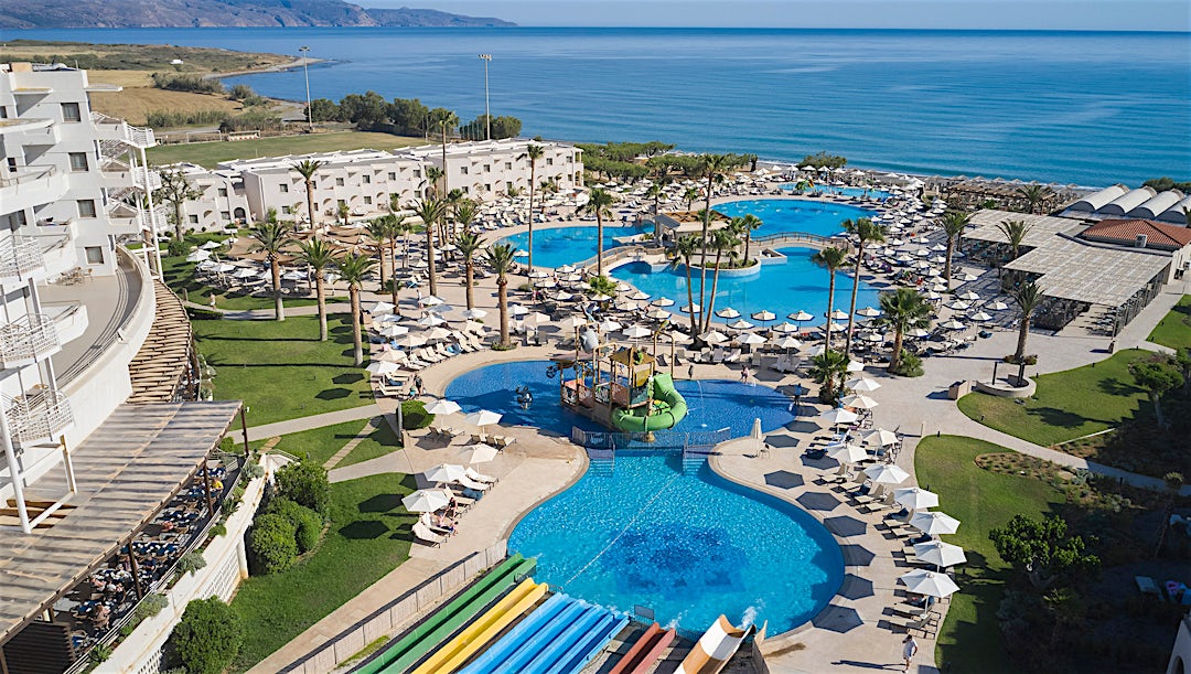 Flygfoto över resort med flera pooler, strandläge och välskötta trädgårdar.