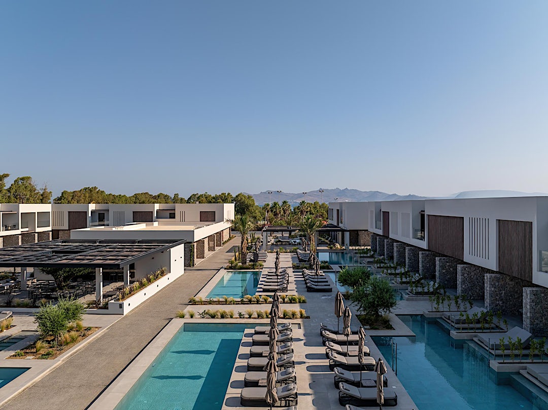 Flygbild över hotellområde med pooler och berg i bakgrunden.